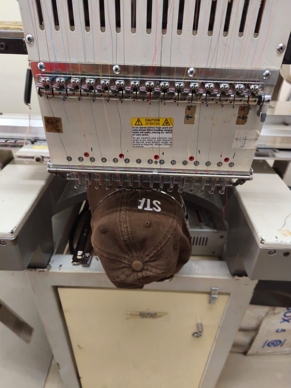 An embroidery machine stitching the STARKBRO lettering onto a brown cap